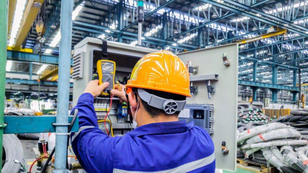 Engineer wearing a hard hat using a multimeter to test electrical components in an industrial facility