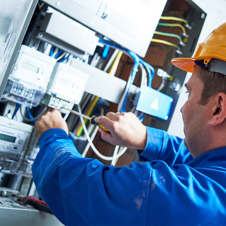 Electrician wearing a hard hat working on an electrical panel with tools.